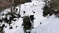 Soldaten in Schneetarnuniform und mit Marschgepäck steigen hintereinander einen Berg hoch.