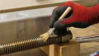 Eine Gewindestange liegt auf einem Holztisch. Ein Soldat reinigt die Gewindestange mit einem Pinsel. Er trägt dabei Handschuhe