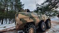 Ein Transportpanzer steht am Ausgang eines Waldstückes.