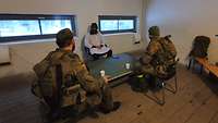 Zwei Soldaten sitzen vor einem großen Tisch. Sie verhören einen ein zivil gekleideten Rollendarsteller.