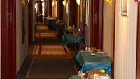 In einem Hotelflur steht neben jeder Tür ein Tisch. Auf diesem stehen Essenstabletts.