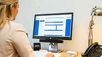 Weibliche Person sitzt am Arbeitsplatzcomputer und befüllt eine Eingabemaske am Monitor