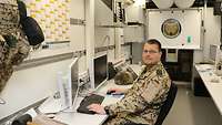 Ein Soldat sitzt in einem Büro innerhalb eines Containers und schaut in die Kamera