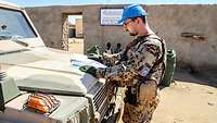 Ein Soldat steht mit seinem Kfz im Gelände und liest eine Landkarte, im Hintergrund stehen einheimische Kinder an einer Mauer