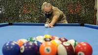 Ein Soldat macht den ersten Stoß beim Billard. Im Vordergrund sind die Kugeln angeordnet.