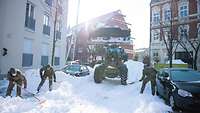 Soldaten schaufeln Schnee auf die Straße. Ein Traktor mit Schaufel steht in Wartestellung.