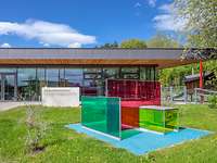 Blick auf ein verglastes Gebäude mit verglasten geometrischen Objekten davor. 