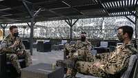 Drei Soldaten sitzen auf einer Rattan-Möbel-Sitzgruppe und unterhalten sich
