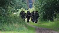 Mehrere Soldaten marschieren in drei Reihen einen Waldweg entlang.
