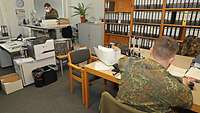 Zwei Soldaten befinden sich in einem Büro mit einem großen Aktenregal.