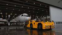 Ein Flugzeug wird mit einem Schlepper in die Halle gefahren