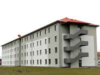 Neues Unterkunftsgebäude Ein großer Neubau mit vier Etagen, rotem Dach und weiß-grauem Außenputz ist fertig.