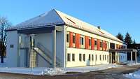 Ein neues zweigeschossiges weißes Gebäude mit roten Fensterläden steht in einer Kaserne.