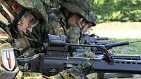 Drei Soldaten liegen nebeneinander auf der Wiese und bedienen Gewehre.