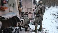 Zwei Soldaten befinden sich zwischen zwei stehenden Fahrzeugen über Geländekarten gebeugt