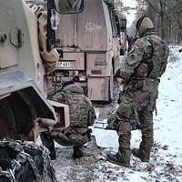 Zwei Soldaten befinden sich zwischen zwei stehenden Fahrzeugen über Geländekarten gebeugt