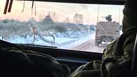 Der Blick durch die Fahrerkabine. Zu sehen ist ein weiteres Fahrzeug, eine verschneite Landschaft und ein Sonnenaufgang