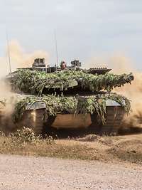Ein Kampfpanzer Leopard fährt durch das Gelände und wirbelt Staub auf