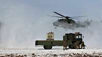 Ein Hubschrauber landet. Hinter einem Lkw suchen Soldaten Schutz. Schnee und Schmutz wird aufgewirbelt.