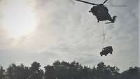 Ein fliegender Hubschrauber transportiert am Seil einen Geländewagen als Außenlast.