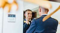 Mann in Uniform steht vor einem Spiegel und bindet sich den Schlips