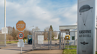 Die Wache Blick auf den Zaun vor einem Wachhaus, rechts steht das Kasernenschild
