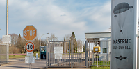 Blick auf den Zaun vor einem Wachhaus, rechts steht das Kasernenschild