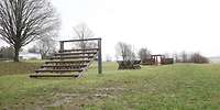 Auf einer Wiese stehen hintereinander mit Abstand verschiedene Holzkonstruktionen.