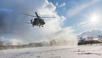 Während sich der Hubschrauber im Landeanflug befindet, wirbelt er Schnee auf. Im Hintergrund: strahlend blauer Himmel