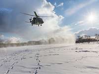 Während sich der Hubschrauber im Landeanflug befindet, wirbelt er Schnee auf. Im Hintergrund: strahlend blauer Himmel