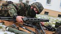 Ein liegender Soldat mit Helm und Ausrüstung zerlegt ein Maschinengewehr auf einer braunen Kokosfasermatte.