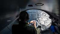 Blick aus einem großen runden Fenster eines Flugzeugs auf eine Wasseroberfläche.