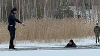 Ein Taucher steht auf dem Eis und gibt einem anderen Taucher, der im Wasser vor ihm schwimmt, Anweisungen.
