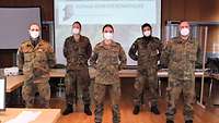 Fünf Soldaten der Bundeswehr stehen mit hinter den Rücken verschränkten Armen in einem Büroraum frontal zur Kamera.