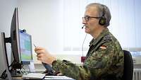 A soldier sits in front of a personal computer and points with a pen onto the monitor while he explains something