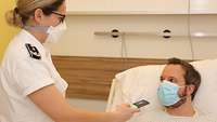Eine stehende Frau hält ein elektrisches Gerät in Richtung eines liegenden Patienten
