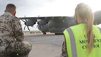 Eine deutsche Soldatin und ein deutscher Soldat beobachten aus der Ferne ein Transportflugzeug 