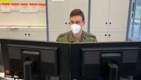 Ein Soldat sitzt hinter zwei Bildschirmen an einem Bürotisch.