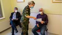 Eine Soldatin teilt einem Patienten mit, dass er die Impfstelle verlassen kann.