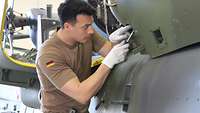 Ein Soldat in Bundeswehr T-Shirt steht an einem Hubschrauber und arbeitet mit einem Schraubendreher 