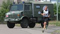 Ein Mann läuft in einer Kaserne, im Hintergrund ein Unimog mit rotem Kreuz an der Seite