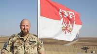 Ein Soldat im Porträt, im Hintergrund weht die Flagge Brandenburgs