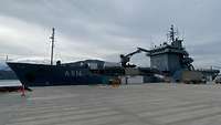Ein Schiff liegt an der Pier und wird mit Material beladen