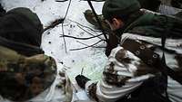 Soldaten hocken über einer Karte, die auf dem schneebedeckten Boden liegt.