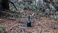 Eine selbstgemachte fiktive Sprengvorrichtung liegt auf dem Waldboden.