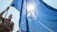 Ein Marinesoldat in sandfarbener Arbeitsuniform hält eine große blaue Flagge.
