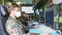 Zwei Soldaten sitzen nebeneinander an militärischer Hardware.