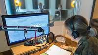 Eine Frau mir Dienstgrad Major sitzt in einem Tonstudio. Sie liefert ihre Stimme für den Sprechertext.