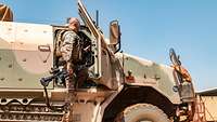 Ein Soldat steigt in sein Fahrzeug ein, er trägt eine Schutzweste und seine Waffe