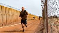 Ein Soldat joggt eine Runde im Camp: Er trägt dabei seine Schutzweste, im Hintergrund gehen zwei weitere Soldaten